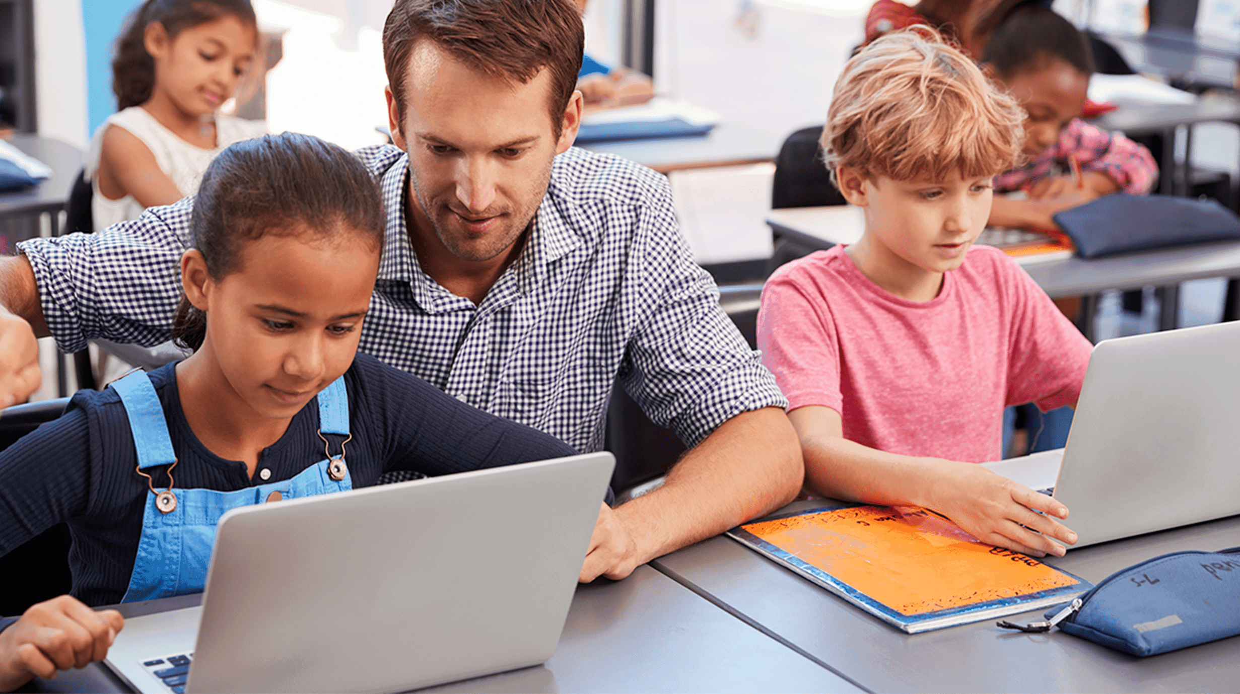 Image of teacher assisting students that are engaged with school work on laptops
