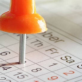 An orange pushpin pierces a calendar page, marking a specific date. The calendar shows days of the week, including Thursday, Friday, and Saturday, with date numbers visible.