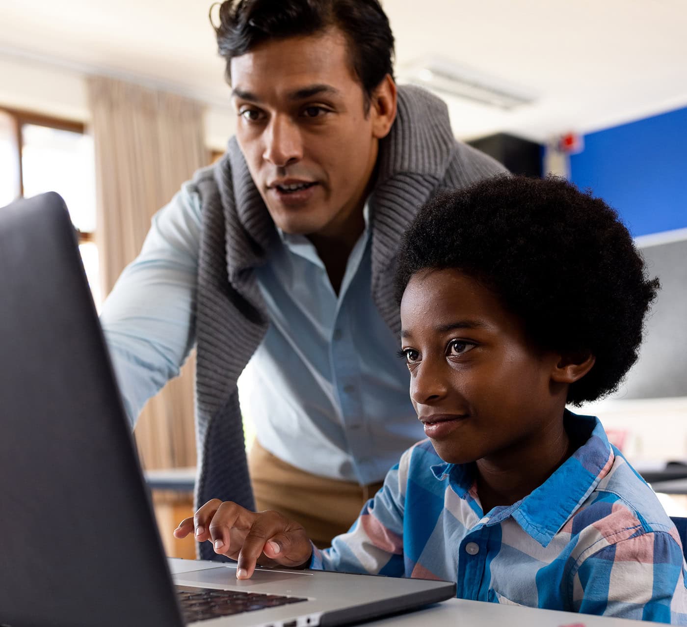Teacher helps student with laptop.