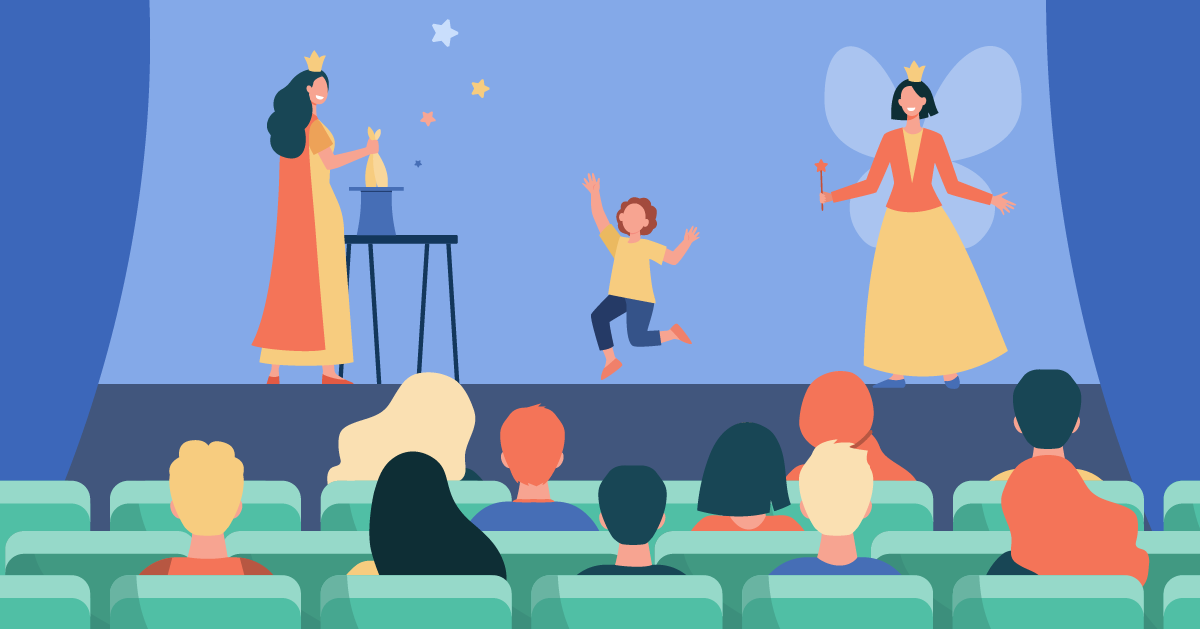 A child joyfully jumps on stage between two performers in costume, one casting spells from a table, the other holding a wand in a theater setting with an audience watching.